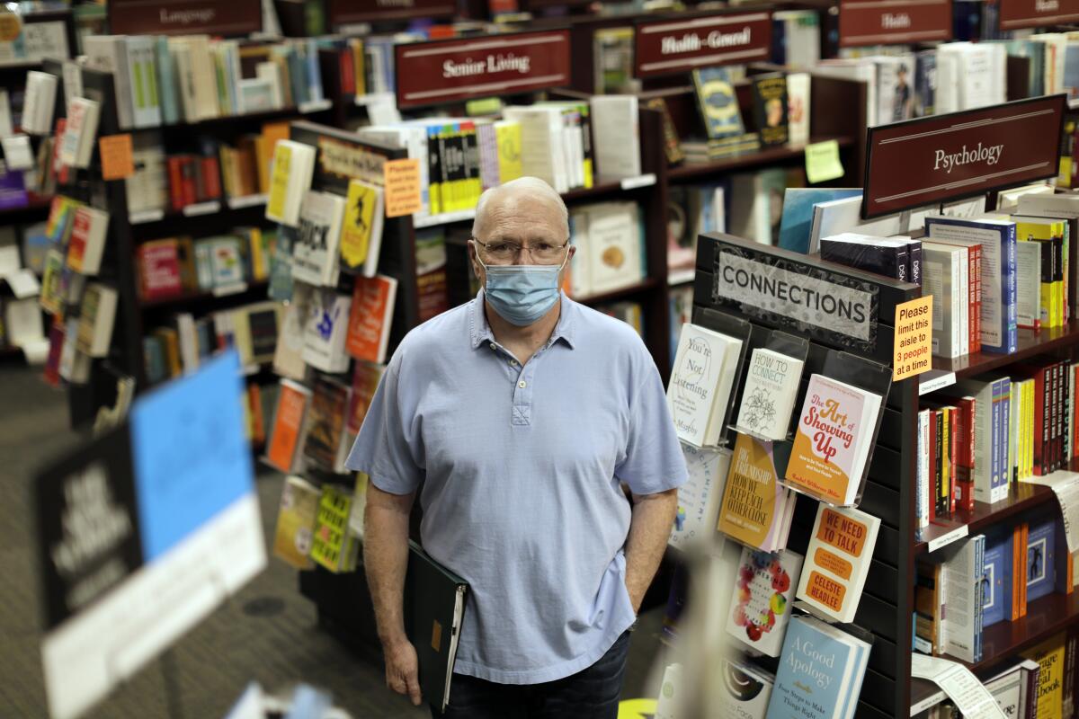 A man wearing a face mask stands among rows of books