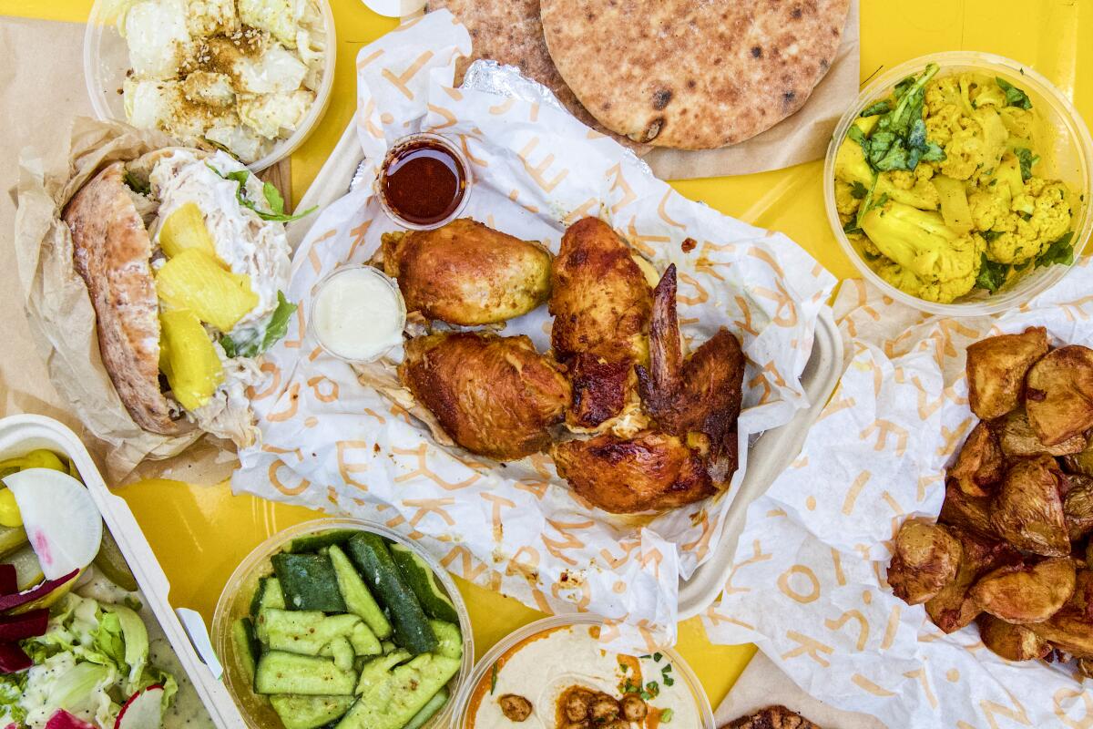 An overhead photo of a spread of chicken and sides from Kismet Rotisserie on a yellow tabletop.