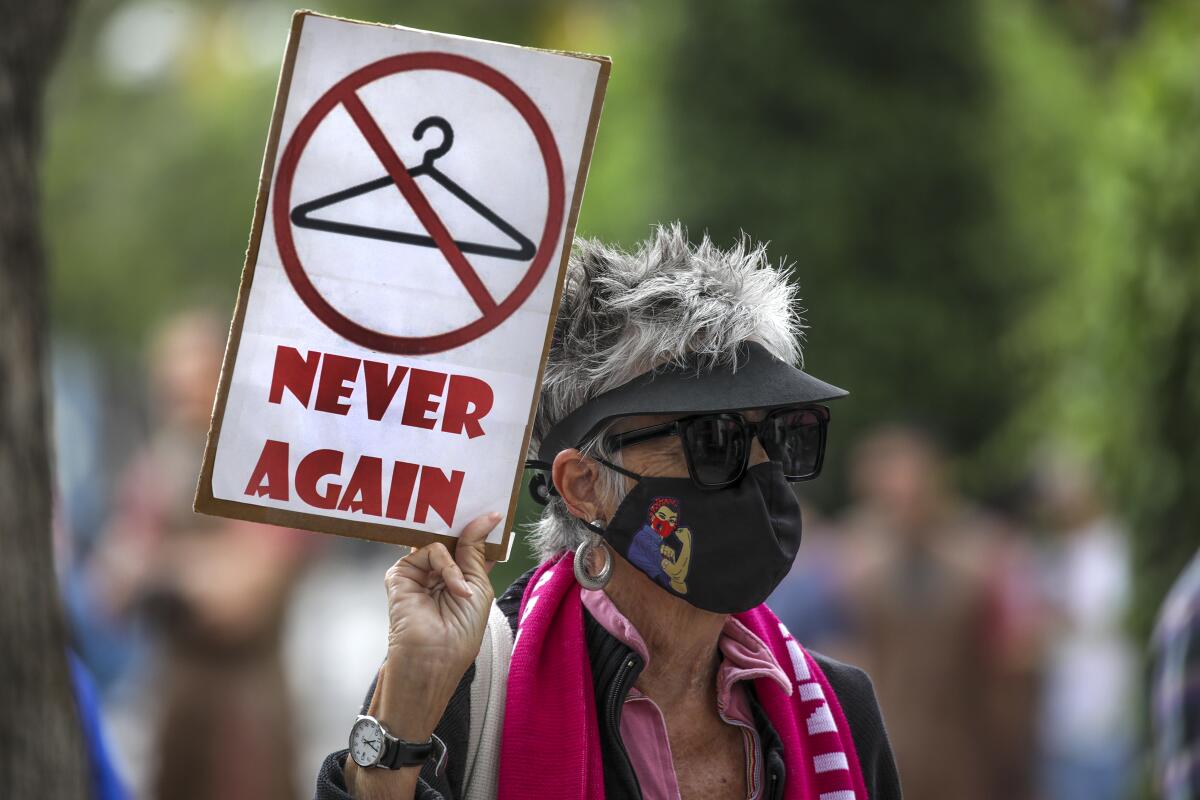 A woman holds a sign that pictures a coat hanger with a slash across it and the words "never again."