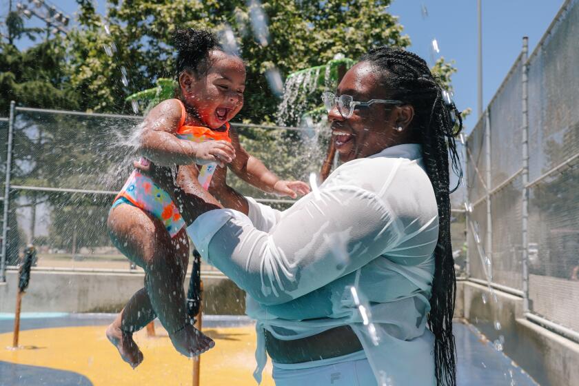 San Fernando Valley, CA - July 02: Takia Davis cools off with daughter Lareina Ramos, 1, at the Sylmar Recreation Center splash pad on Tuesday, July 2, 2024 in San Fernando Valley, CA. A heat wave is expected to bring dangerous temperatures through the Fourth of July holiday and into early next week in many areas. (Dania Maxwell / Los Angeles Times)