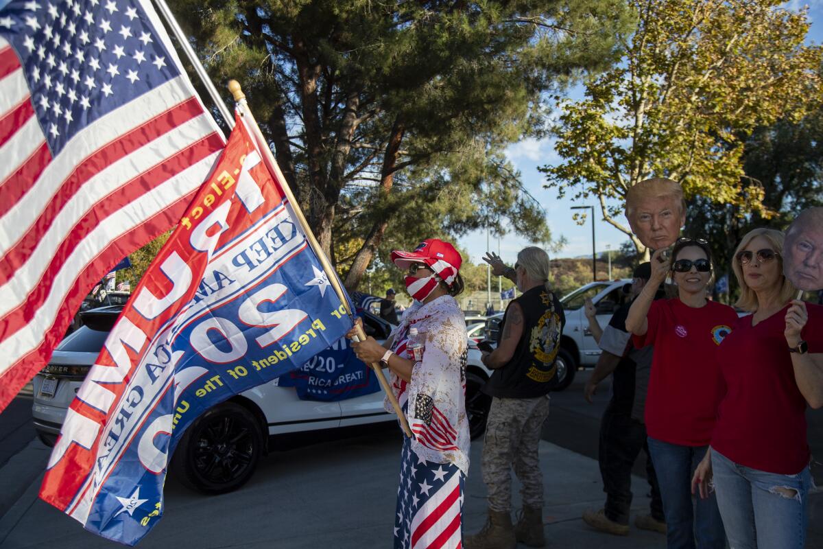 A person with U.S. and Trump 2020 flags as a pro-Trump group waves to passing cars