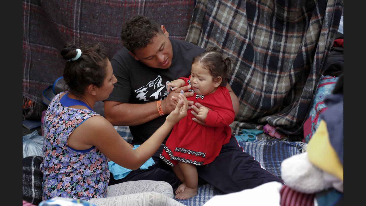 Sheltered at the Benito Juarez Sports Complex Angel and Everlina give their daughter Ashley her medication. The family has been traveling with the Central American migrant caravan from Honduras to Tijuana and among the thousands of asylum seekers.