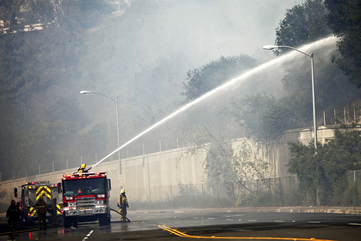 Firefighters on Harvey Drive hose down brush along the Glendale Freeway as a fire burns in the area.
