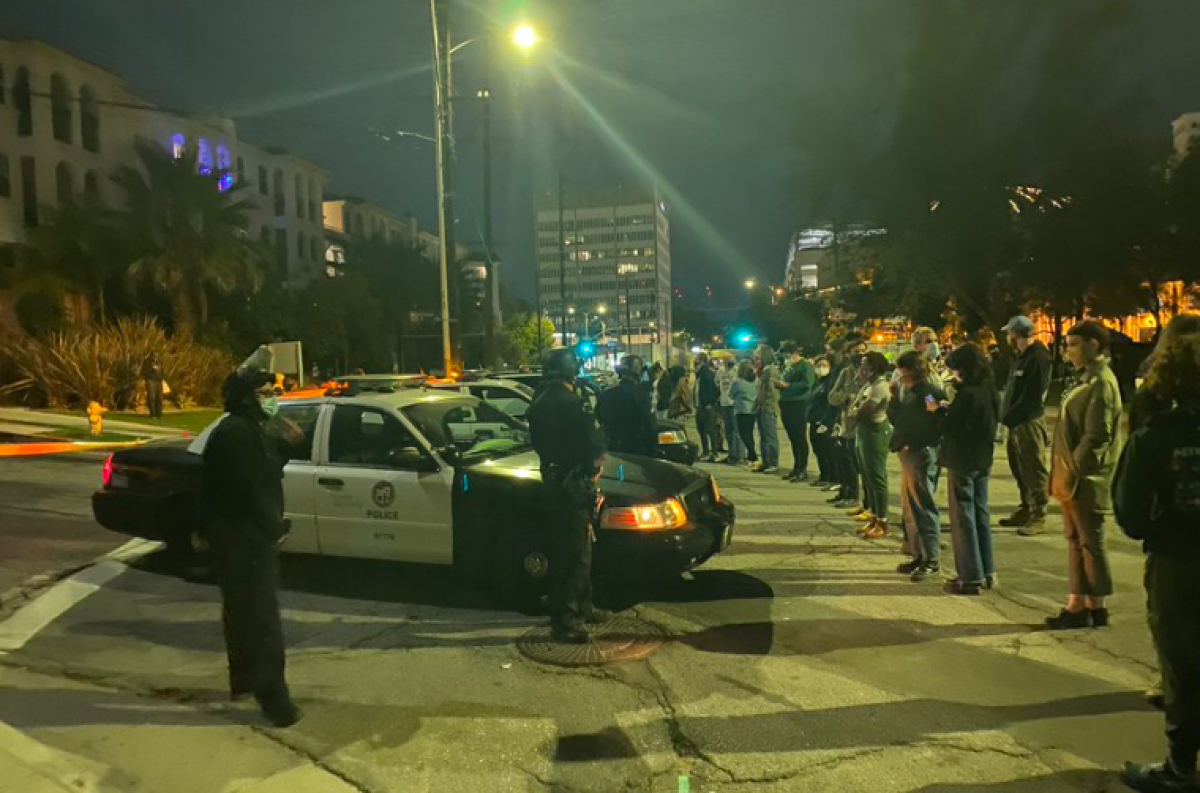 A row of police officers and police cruisers block access to a street leading to Echo Park Lake.