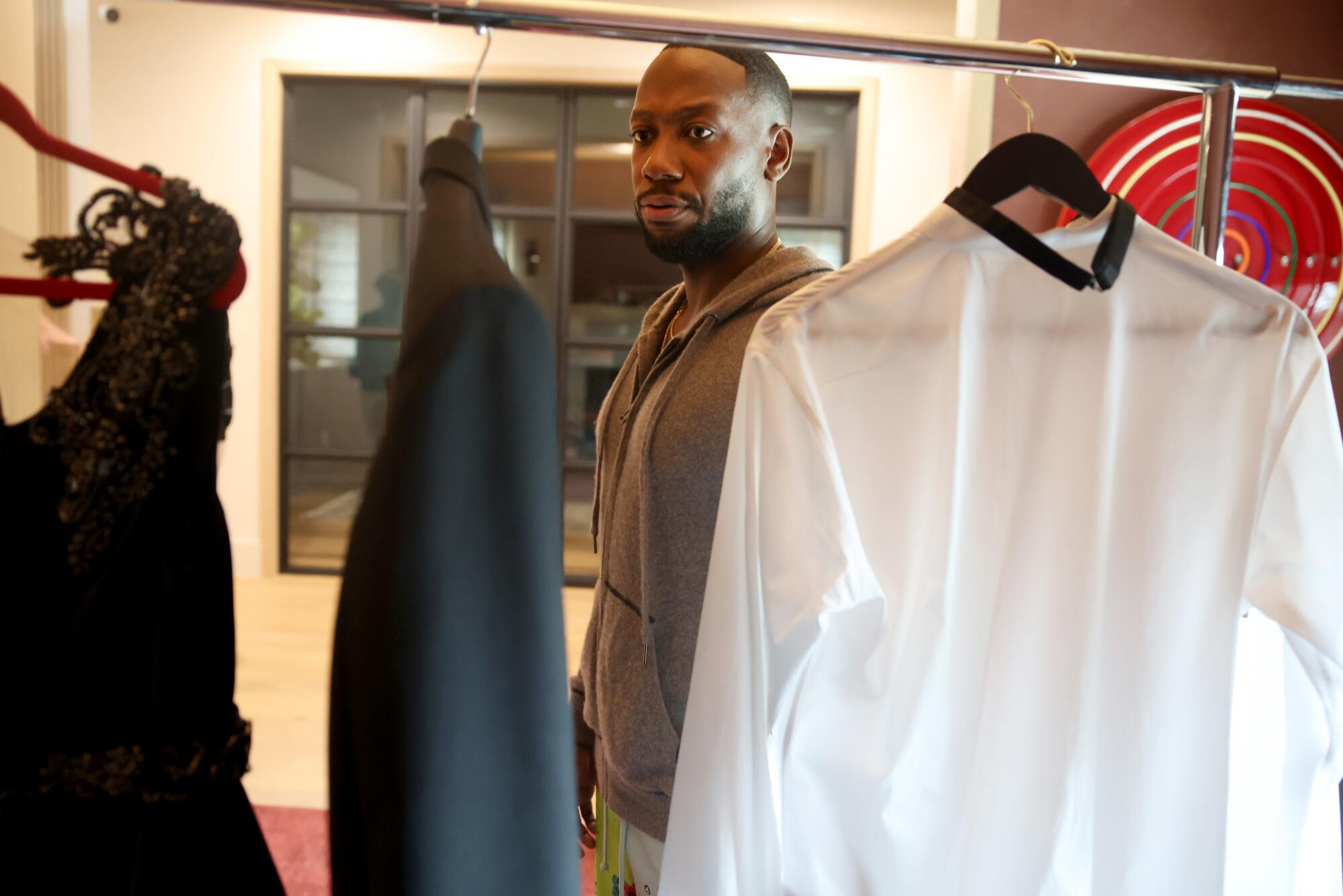 A man walking past a rack with a dress, jacket and white shirt hanging on it.