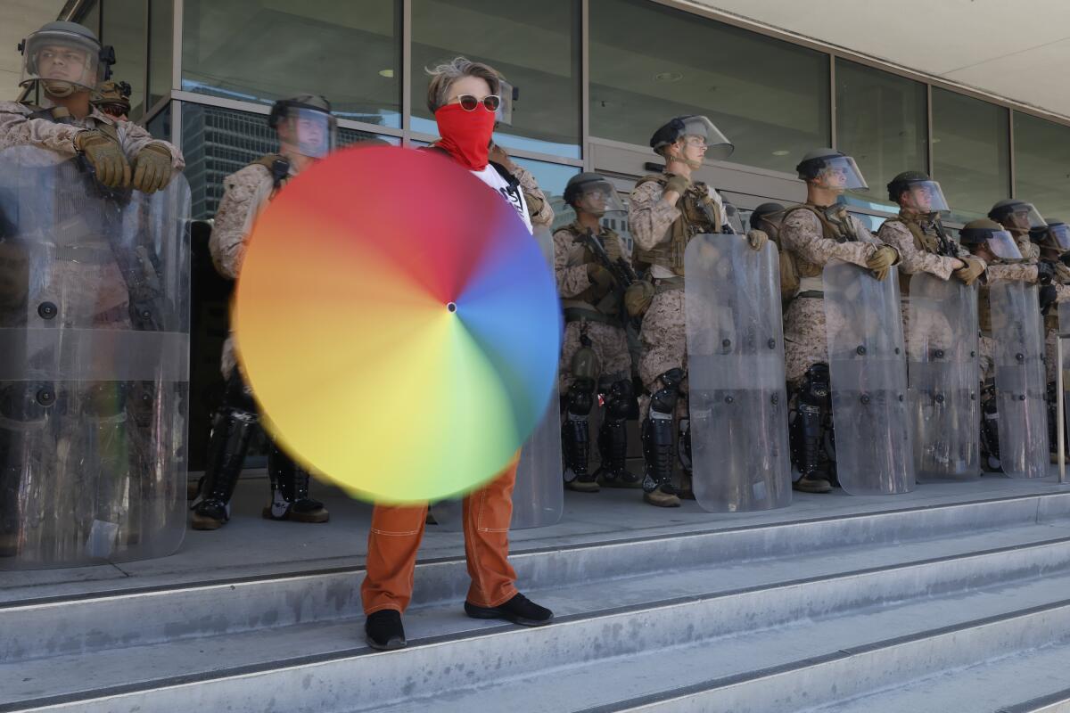 A masked woman spins a rainbow umbrella in front of Marines.
