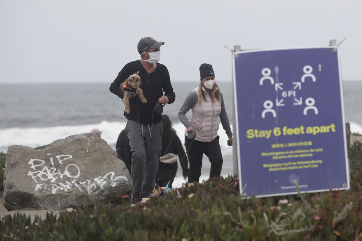 Chris and Pamela McDonnell, both wearing protective face coverings, take their dogs on a closed stretch of the Great Highway at Ocean Beach in San Francisco.