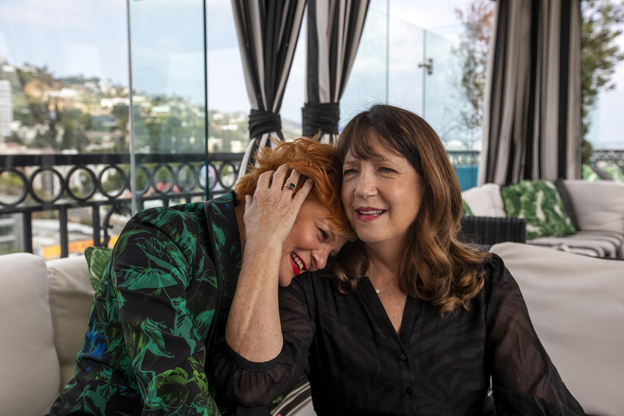 Martha Plimpton nuzzles Ann Dowd on a couch. They co-star in the indie drama "Mass."