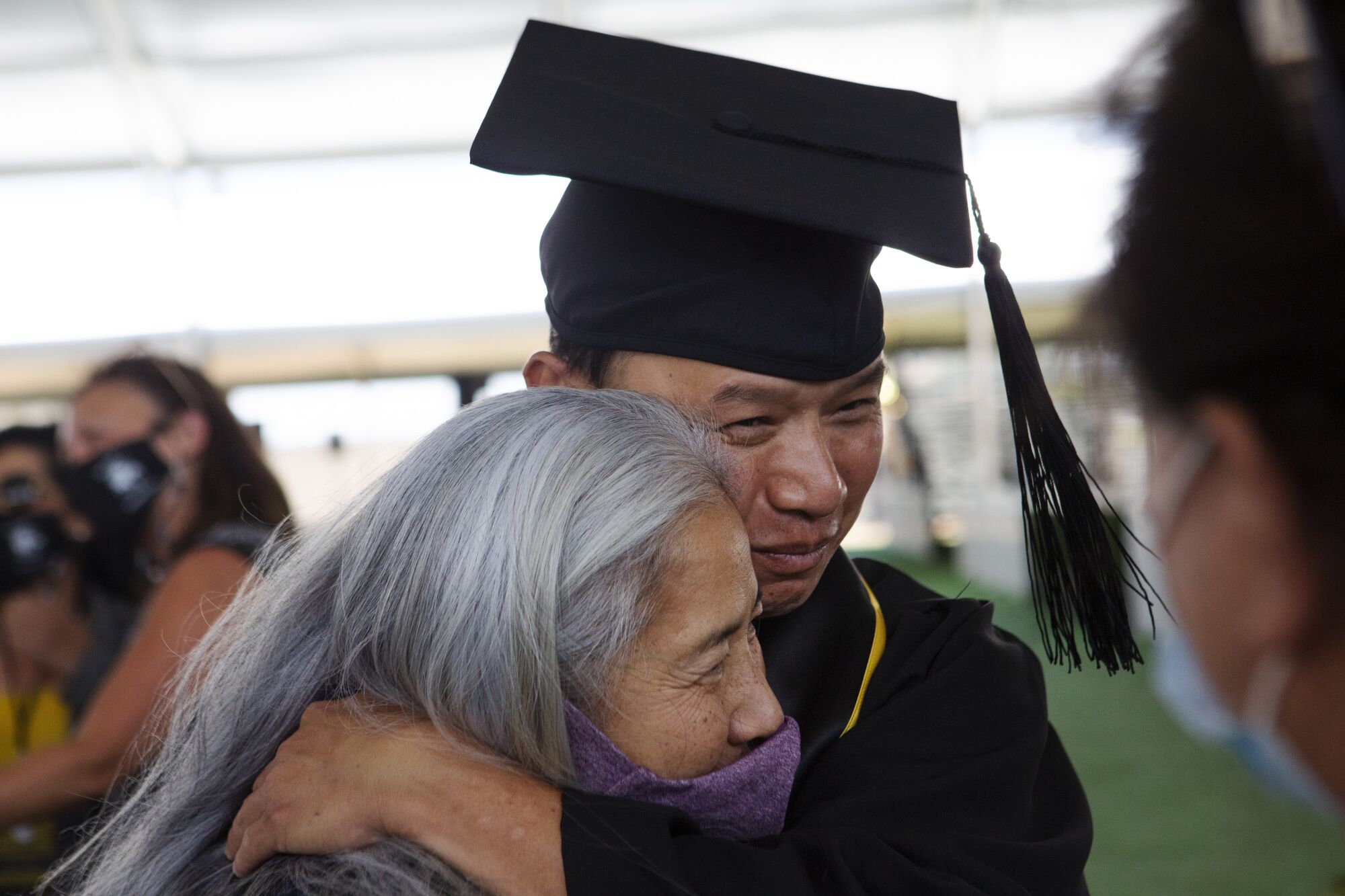 Tin Nguyen, in graduation cap and gown, hugs his sister.  