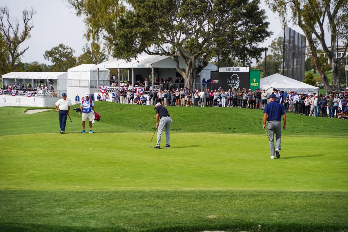 Golfers putt a final stroke as the crowd gathers to watch from hospitality tents.