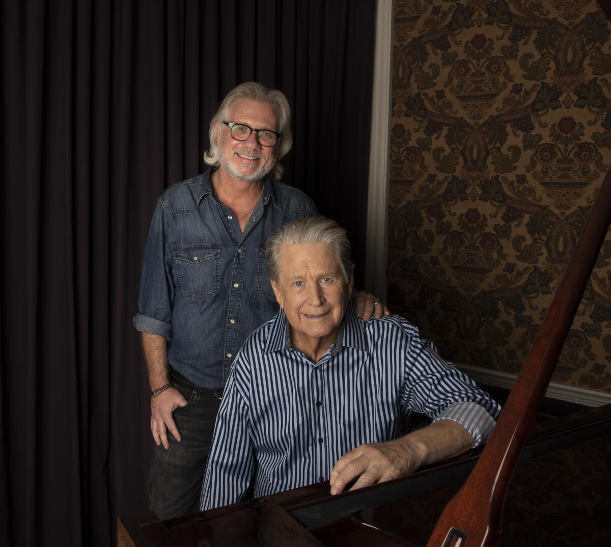 Former Beach Boy Brian Wilson sits at his piano with filmmaker Brent Wilson (no relation) standing behind him.