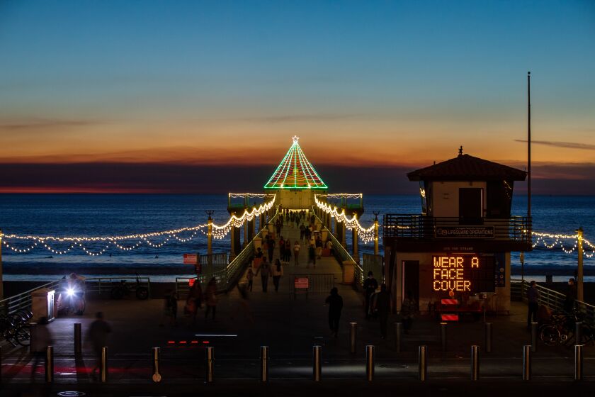 MANHATTAN BEACH, CA - DECEMBER 03: With annual holiday decorations on display, a city sign alerts visitors to the Pier in Manhattan Beach, CA, that face coverings are required, or face up to a $350 fine, on Thursday, Dec. 3, 2020. Due to increases in COVID-19 cases across Southern California, the city of Manhattan Beach is requiring anyone out in public to wear a face covering, or face fines. (Jay L. Clendenin / Los Angeles Times)