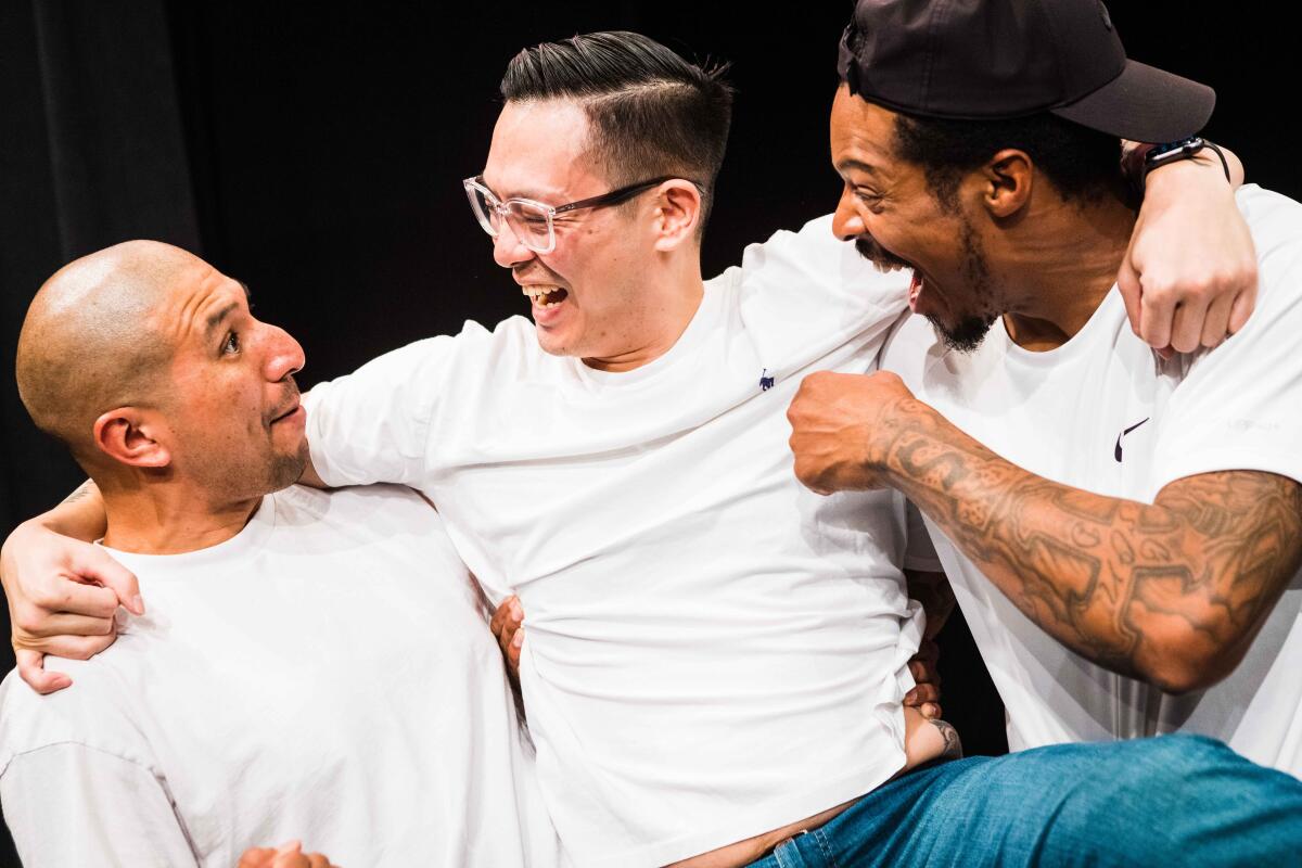 Three actors in jeans and white T-shirts, play a theatrical scene in which they laugh and embrace