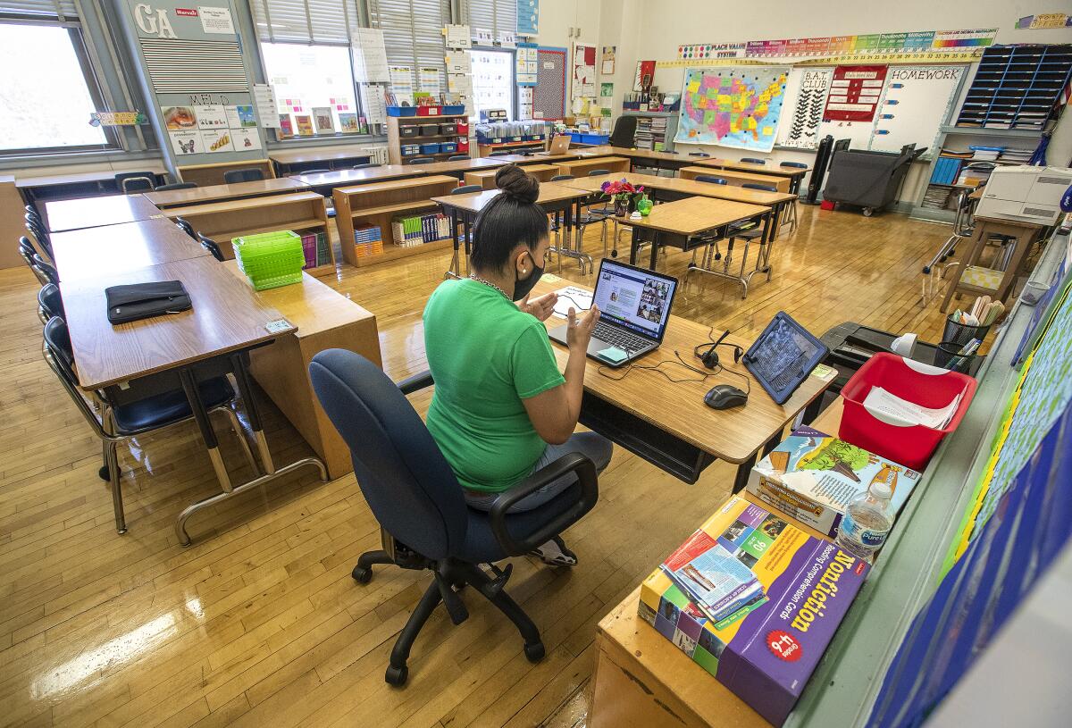 A teacher in an empty classroom talks to students through a computer