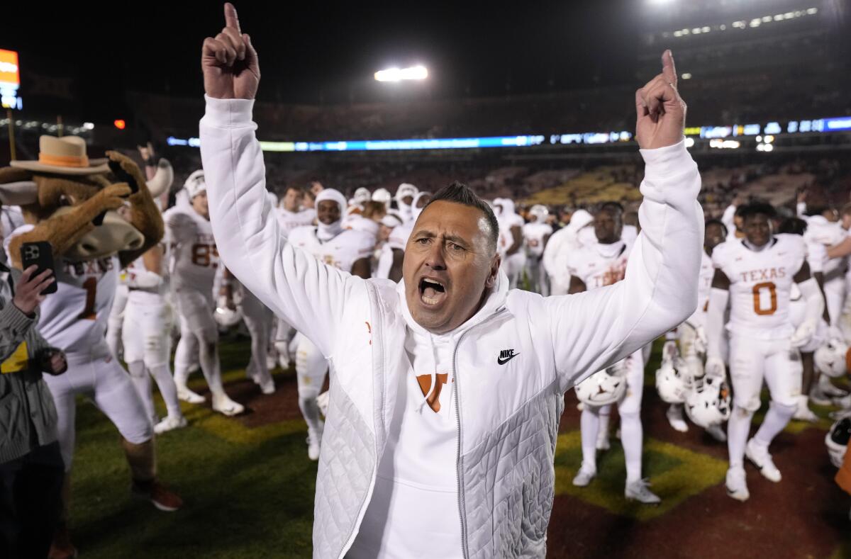 Steve Sarkisian raises his arms and shouts on the field.