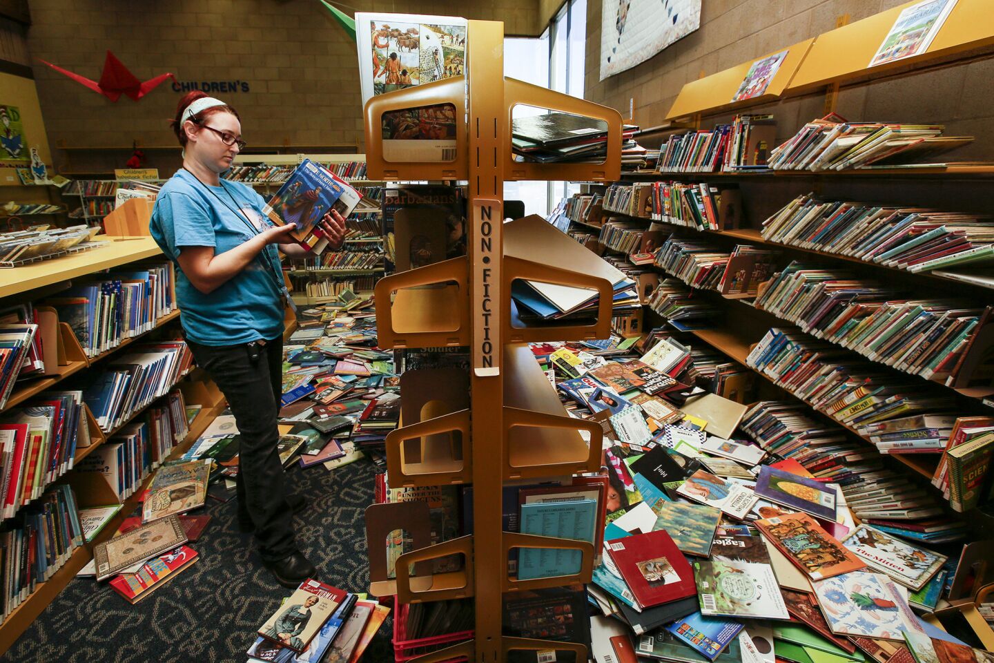 Shalyn Pineda, regional supervisor of Kern County's libraries, picks up books at Ridgecrest Library after Thursday's 6.4 earthquake dislodged bookshelves.