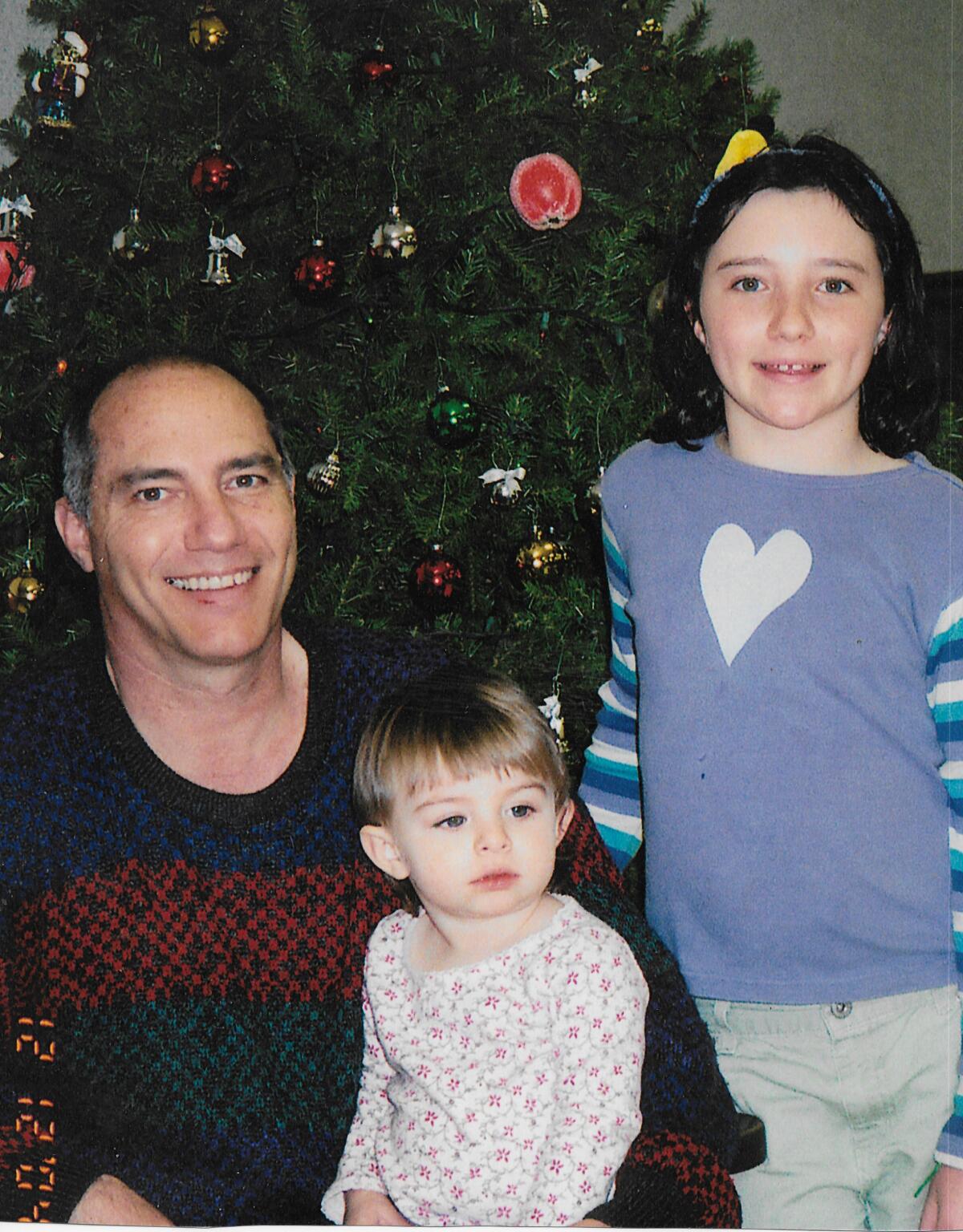 Patrick Burns smiles by a Christmas tree with his daughters.