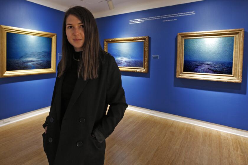 Laguna Art Museum teaching artist Ina Rosca poses in front of night scenes by painter Granville Redmond, at the museum in Laguna Beach on Friday, Sept. 11, 2020.