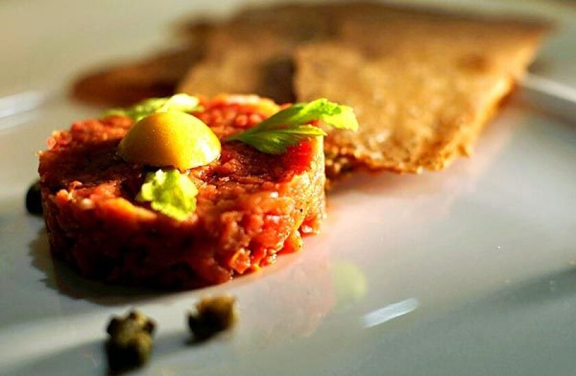 Tomato tartare mimics steak tartare with a flat patty of diced tomatoes and yellow tomato on top standing in for an egg yolk.