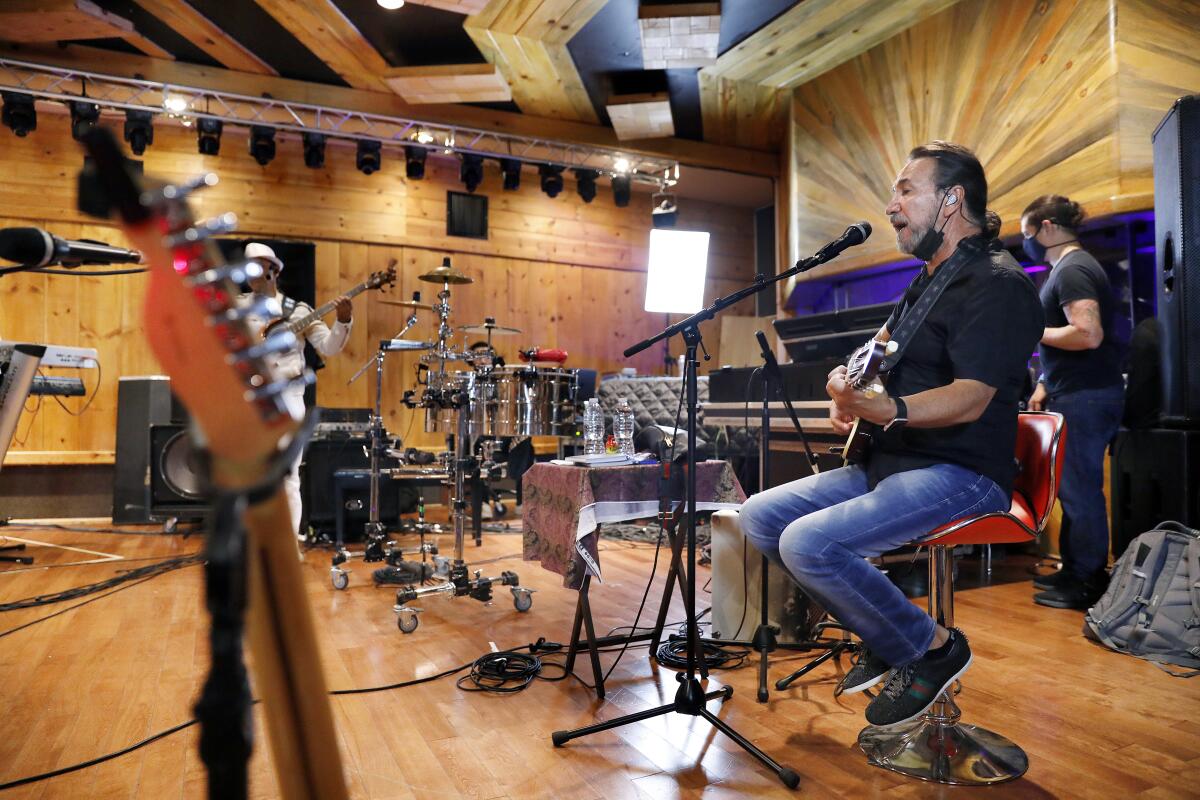 A man plays a guitar inside a studio next to a drum setup 