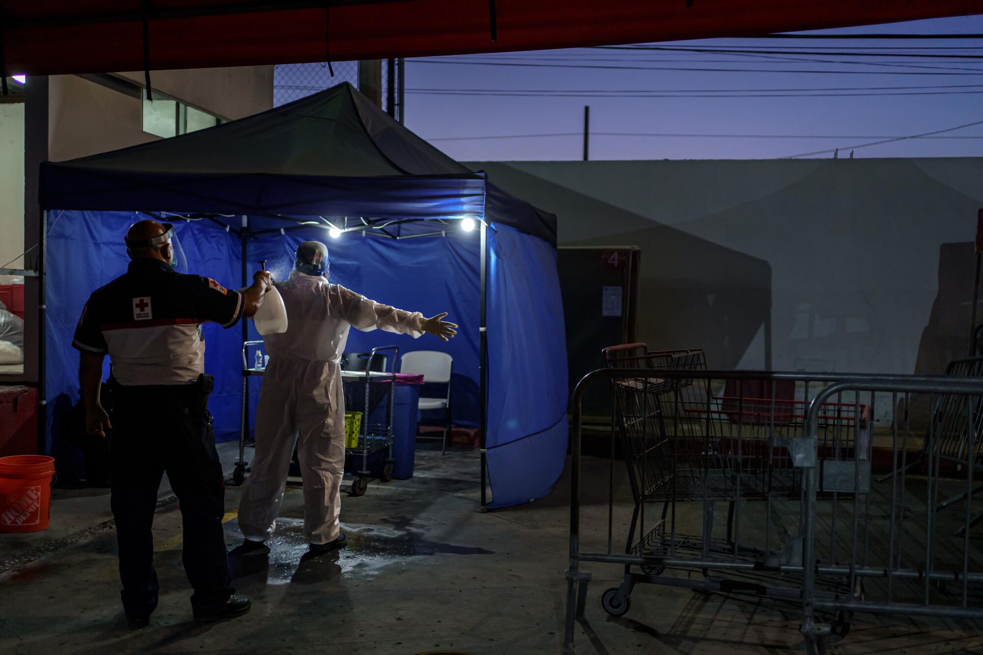 Ulises Rodriguez, the Chief-on-duty, left, supervises a decontamination and removal of personal protective equipment after paramedics complete an emergency call or medical transport related to COVID-19, at the Red Cross base in Tijuana, Mexico, on May 2, 2020.