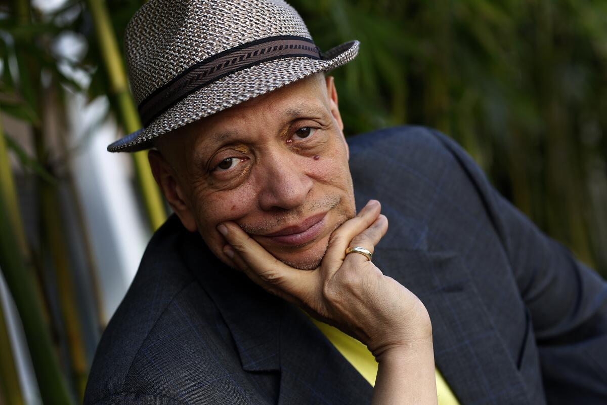 A man wearing a fedora poses with his hand under his chin.