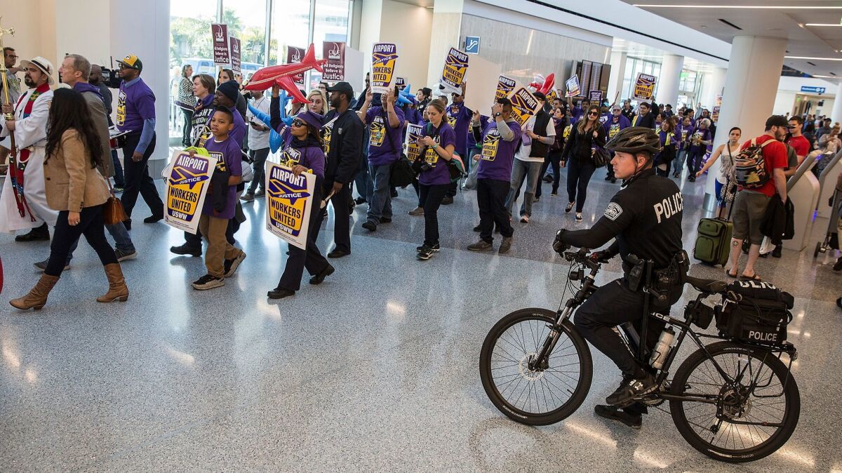 Police watch as workers and supporters march for higher pay and union representation through the terminals at Los Angeles International Airport.