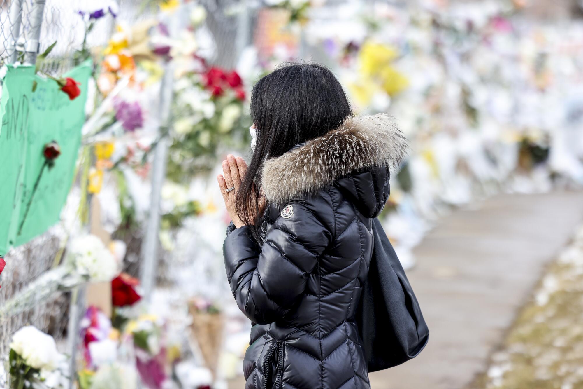 A woman stands with her hands clasped in front of a display of flowers on a sidewalk