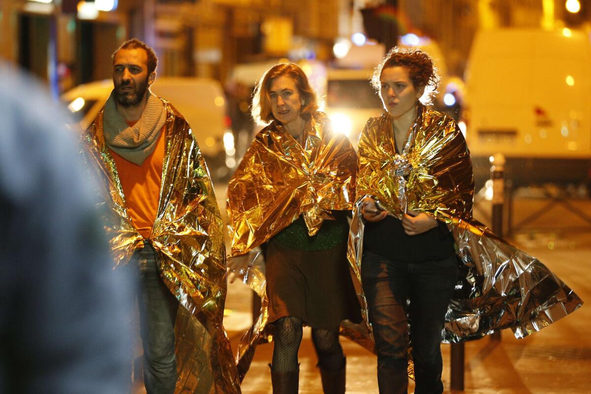People wrapped in emergency blankets walk near the Bataclan concert hall early Saturday morning.