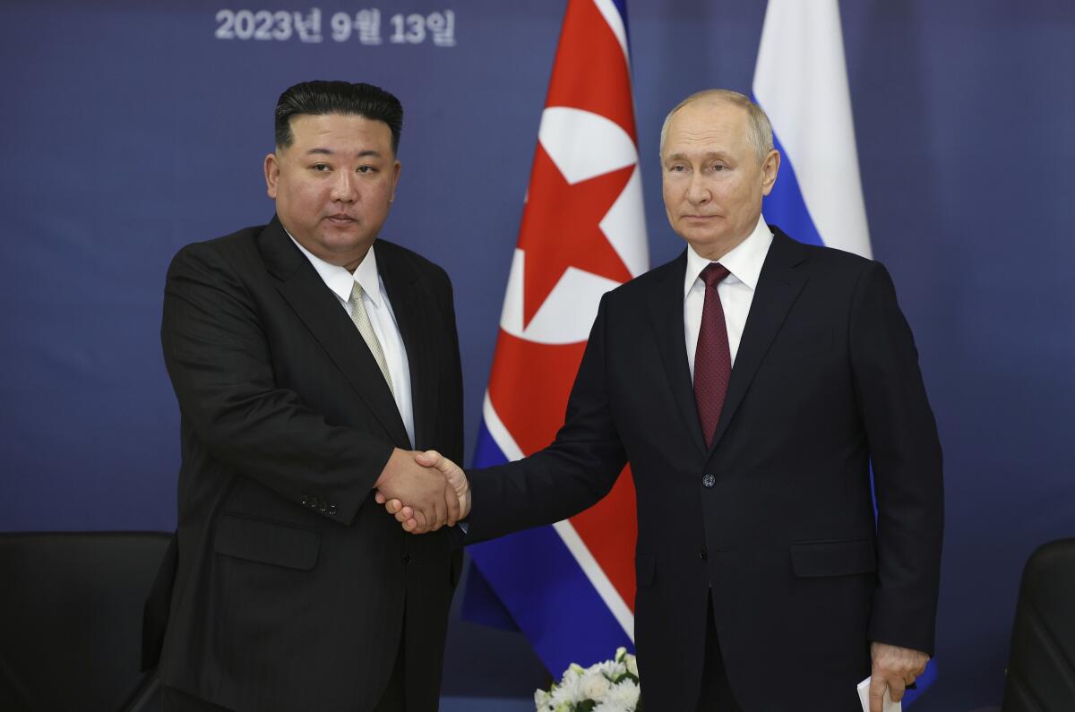 Russian President Vladimir Putin and North Korea's leader Kim Jong Un shake hands in front of flags.