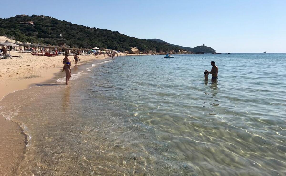  personas disfrutando de la arena y el agua en la playa Chia, en la isla italiana de Sardinia, Italia