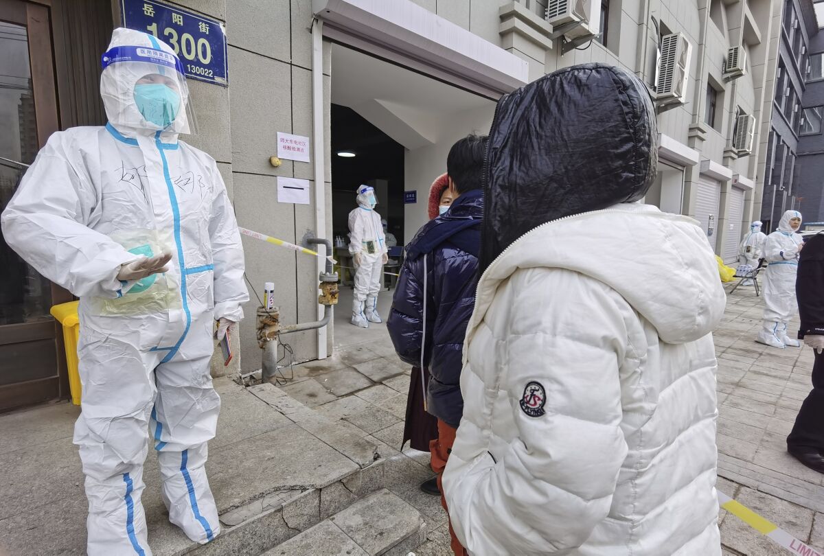 A worker wearing a protective suit speaks to residents in a neighborhood in Changchun in northeastern China's Jilin Province, Friday, March 11, 2022. China on Friday ordered a lockdown of the 9 million residents of the northeastern city of Changchun amid a new spike in COVID-19 cases in the area attributed to the highly contagious omicron variant. (Chinatopix via AP)