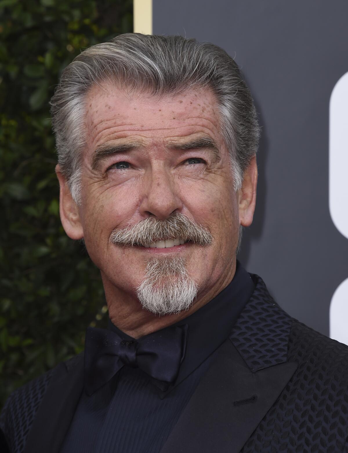 Pierce Brosnan with a mustache and goatee smiling