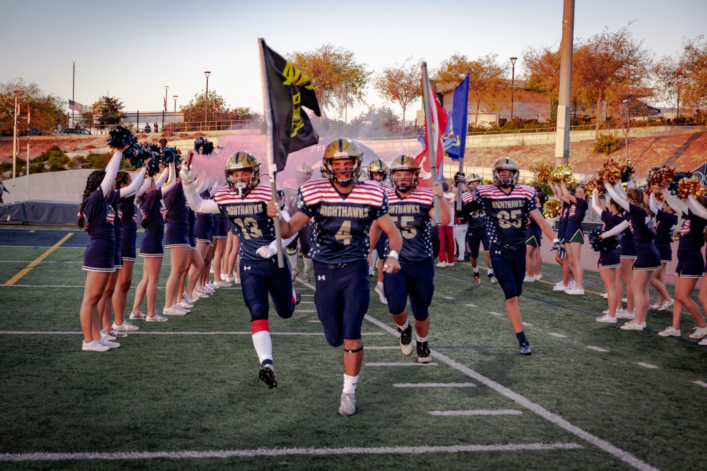 Players Khalid Farah (4), Kyle Stephenson (13), Mason Gizicki (55), Ryan Goldstein (85), run out of the tunnel holding flags representing each branch of the military and Navy, and red, white, and blue smoke grenades.