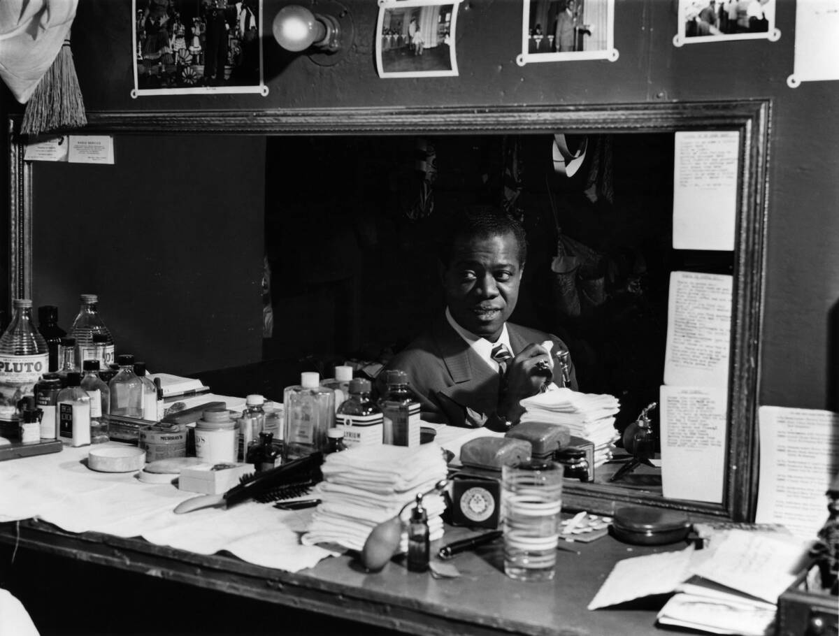 Louis Armstrong reflected in a mirror, seated at a dressing table