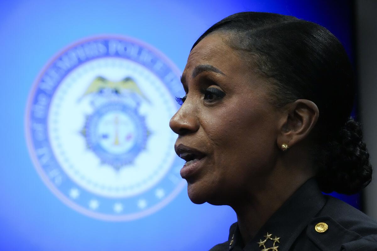 A closeup of a woman in a police uniform, with a blurry police logo in the background