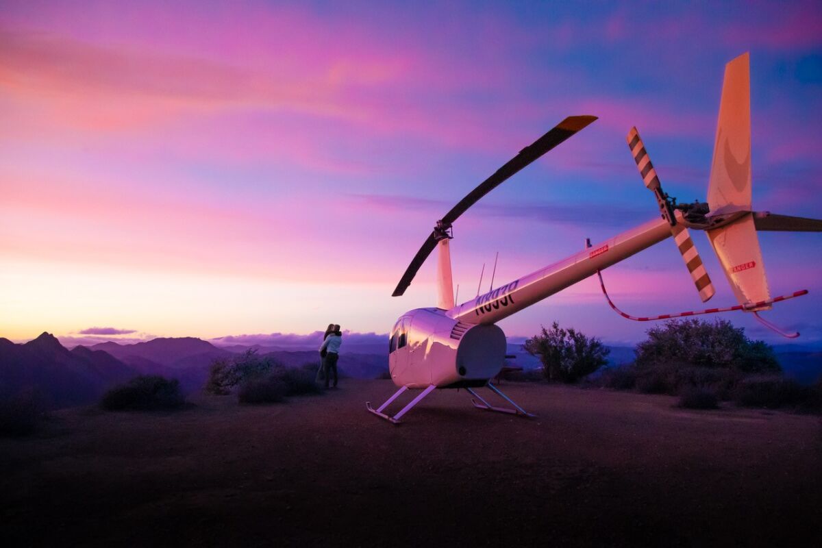 A helicopter with a couple hugging in the background at sunset.