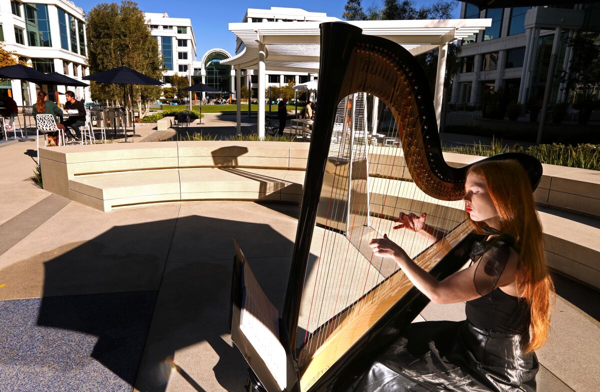 a woman with long red hair plays a harp in a green courtyard at an office complex