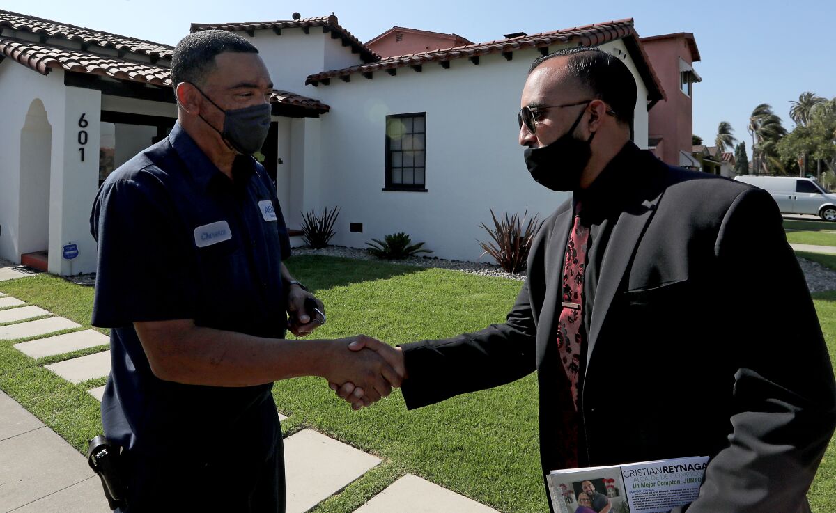 Two men wearing masks shake hands outside a house