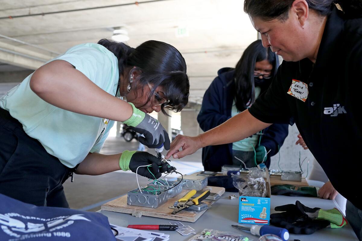 Kim Camacho-Pacheco, left, an Estancia High  student, learns to build a switch receptacle, guided by Erica Torres, right.