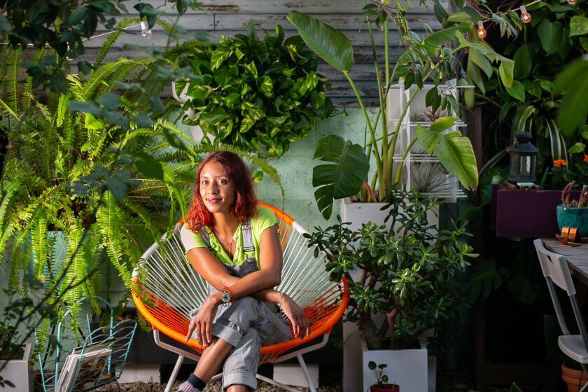 Chantal Aida Gordon sits in an orange Acapulco chair in her patio garden.