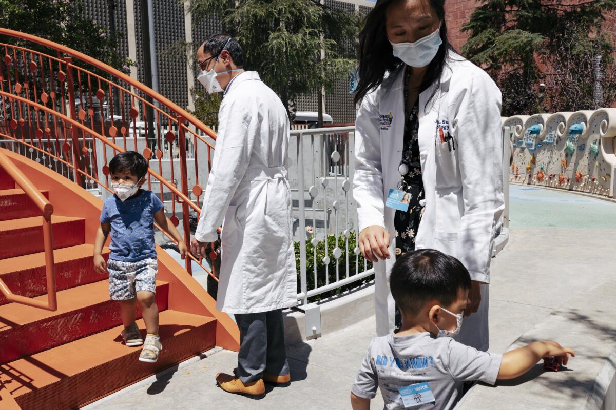 Children wait with hospital staff in white coats, everyone wearing masks