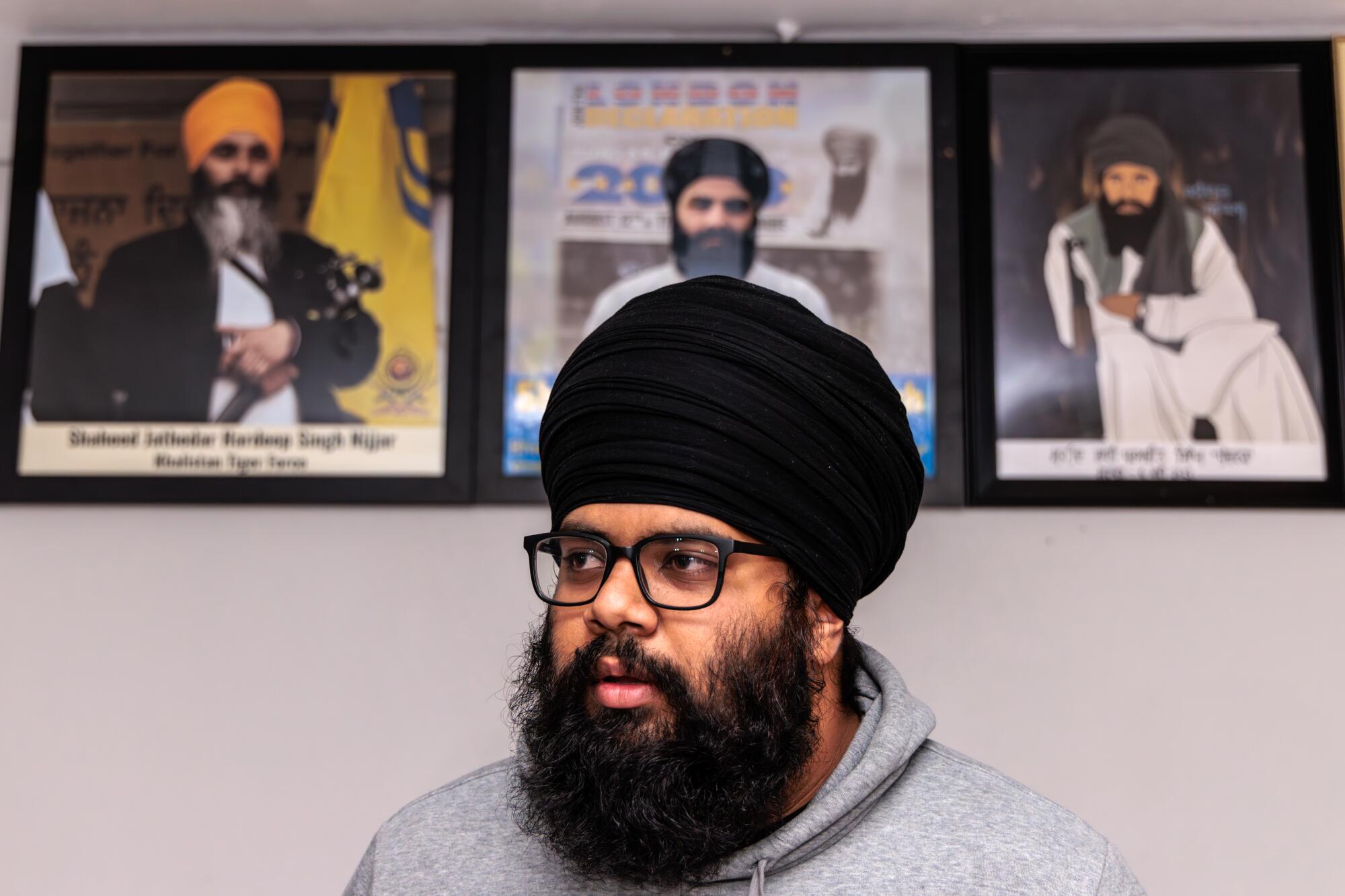  A man with a dark beard, glasses and a dark turban is shown with portraits of three turbaned men behind him