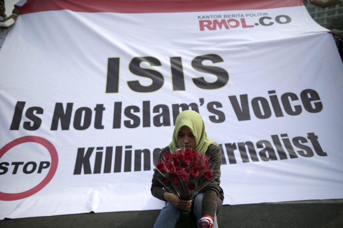 An Indonesian journalist holds flowers as she sits in front of a banner during a protest in Jakarta against the killing of journalists by Islamic State.