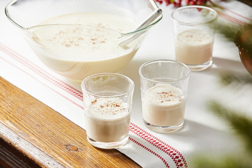 A punch bowl and glasses on a table hold Deluxe Eggnog.