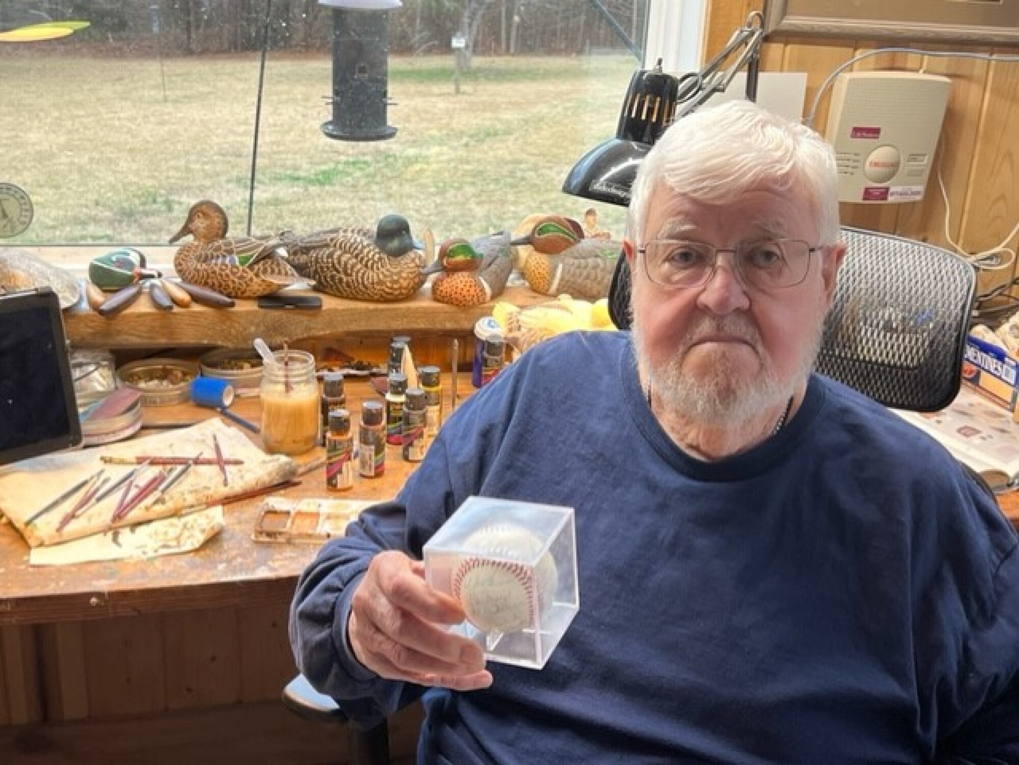 Denny Lemaster holds a baseball while sitting in front of some of the duck decoys he carved and painted.