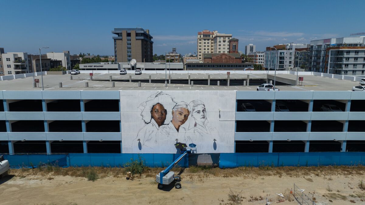 A bird's eye view shows a mural of three figures coming together on the side of a parking structure in Long Beach.