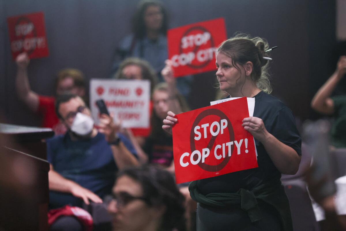 People in a meeting hall hold signs that say "Stop Cop City!"