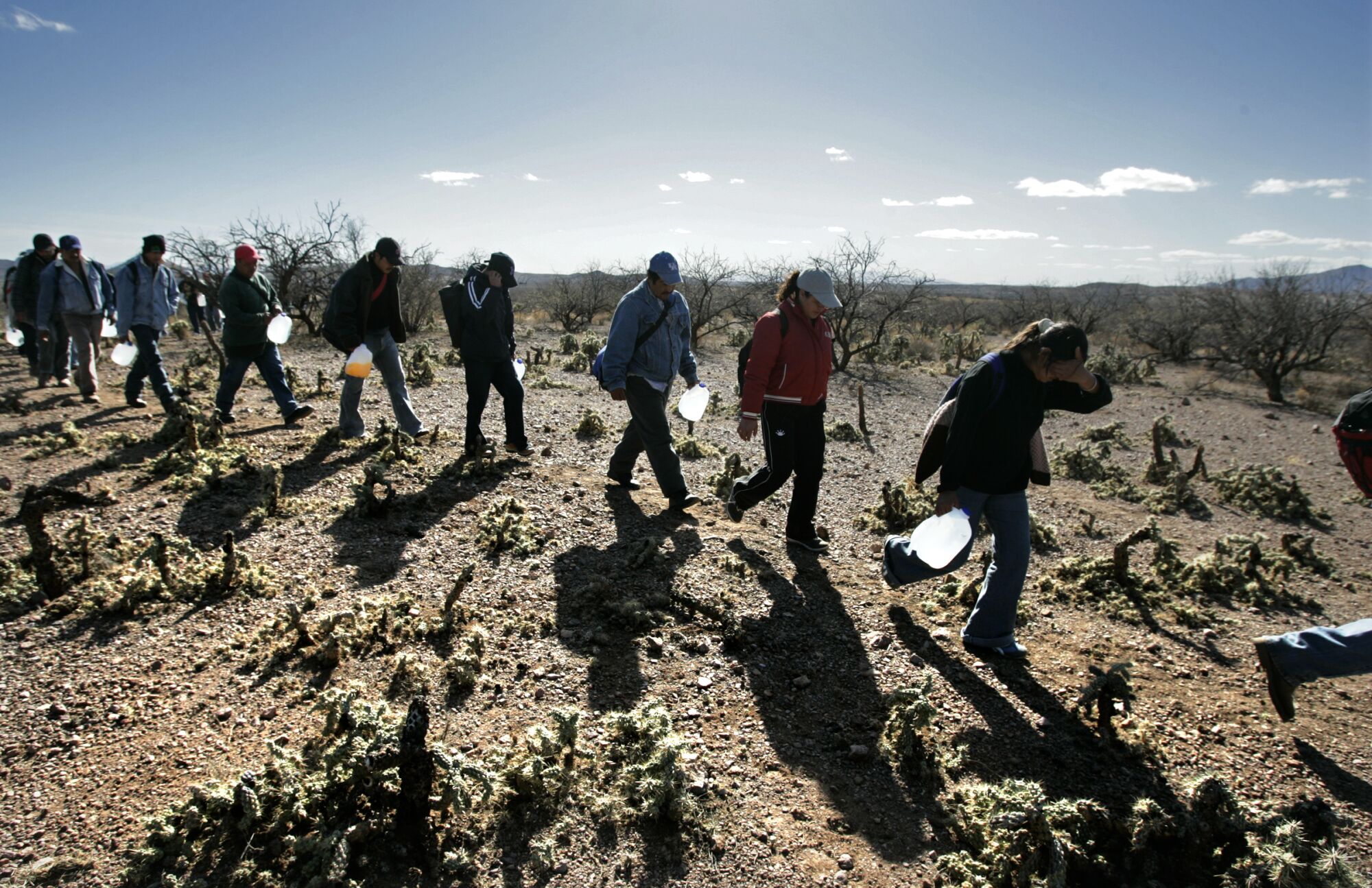 Lugging gallon jugs of water, migrants thread their way along footpaths just north of the Mexico-Arizona border. 
