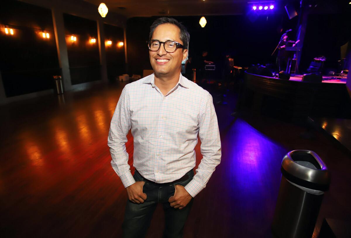A man in a button-down and glasses smiles in a dark ballroom